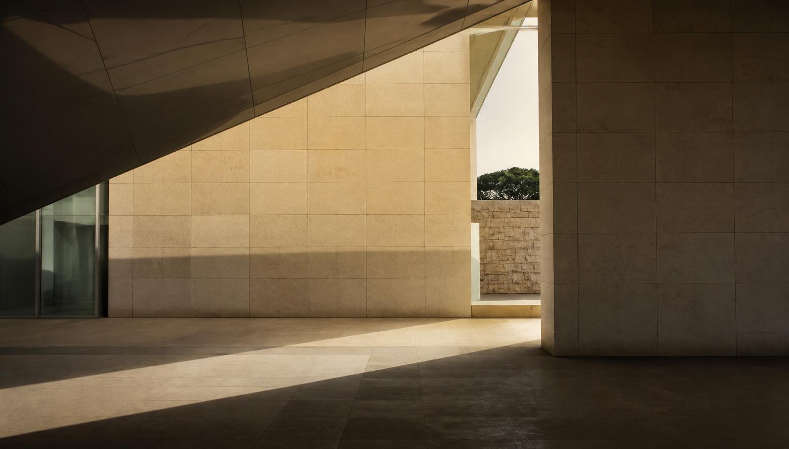 Intersecting limestone and glass planes of a modern building, one opening revealing unexpected depth beyond